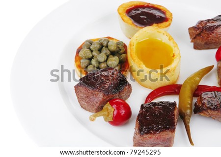 european food: roast beef meat goulash over round white plate isolated over white background with red hot pepper, capers and sauces