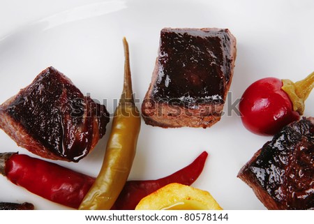 european food: roast beef meat goulash over round white plate isolated over white background with red hot pepper, capers and sauces