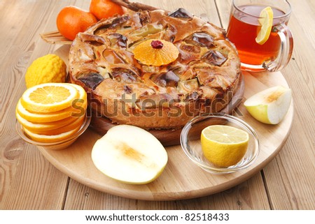 baked food : big apple pie served with fresh apples, raw lemon and mandarin,  tea cup on wooden plate over table