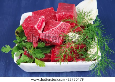 uncooked fresh beef meat chunks on white bowls with green hot peppers and vegetables serving over blue wooden table