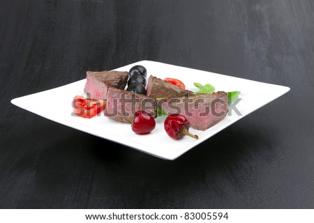 meat food : roasted fillet mignon on white plate with tomatoes apples and chili pepper over black wooden table