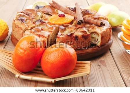 baked food : apple pie served with fresh apples, raw lemon and mandarin,  tea cup on wooden plate over table