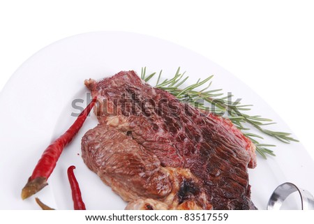 meat food : grilled beef steak served on white plate with red thin chili pepper and spices isolated over white background
