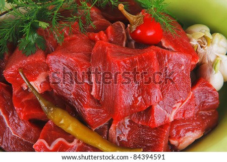 uncooked fresh beef meat chunks on ceramic bowls with vegetables and red peppers isolated over white background