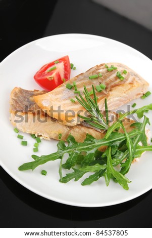 savory sea fish : roasted salmon fillet garnished with green rocket leaves and tomatoes on black dish isolated over black background