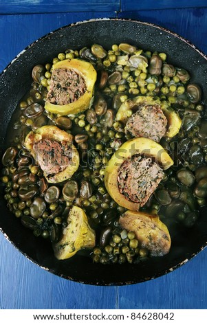homemade cuisine: zucchini filled meat with peas, beans on black used pan over blue wood