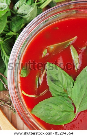 diet food : hot tomato soup with basil thyme and raw tomatoes in transparent bowl over red mat on wood table ready to eat