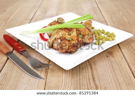 roast meat : roasted chicken legs garnished with green peas , peppers , and garlic on white plates over wooden table