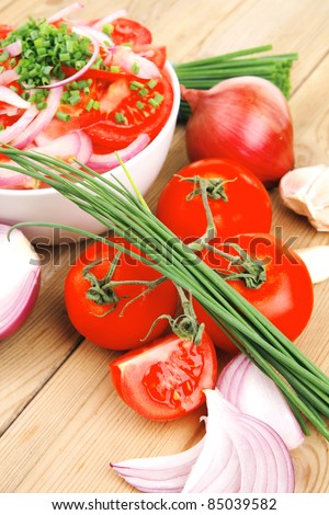 healthy food : fresh tomato salad in white bowl with bunch of chives and raw tomatoes on twig , onion, and garlic over wooden table