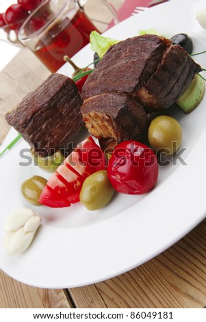 grilled meat : beef ( lamb ) garnished with tomatoes , green and black olives, tomatoes and juice on wooden table