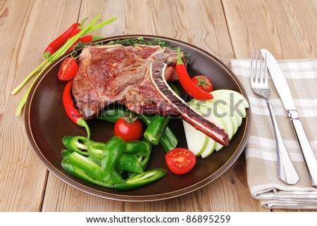savory : roasted beef spare rib on dark dish with cutlery thyme pepper and tomato on wooden table