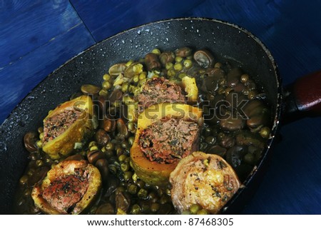 homemade cuisine: zucchini filled meat cooked with peas on black pan over blue