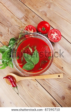cold fresh diet tomato soup with basil thyme and raw tomatoes in transparent bowl over red mat on wood table ready to eat