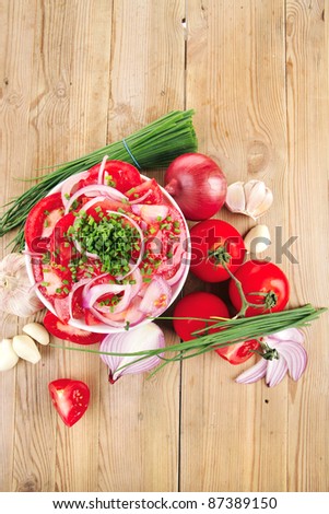 healthy appetizer : fresh tomato salad in white bowl with bunch of chives and raw tomatoes on twig , violet onion, garlic over wooden table