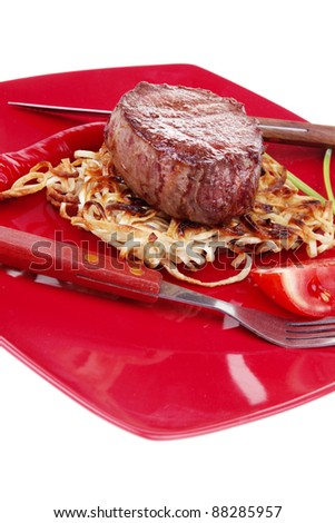 grilled beef fillet pieces on noodles , red hot chili pepper and tomato on red plate isolated over white background