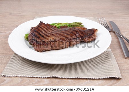 meat table : grilled beef fillet with asparagus served on white plate with cutlery over wooden table