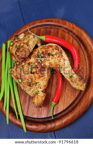 meat food : roasted chicken legs garnished with green onion pens and peppers on wooden plate over blue wooden background