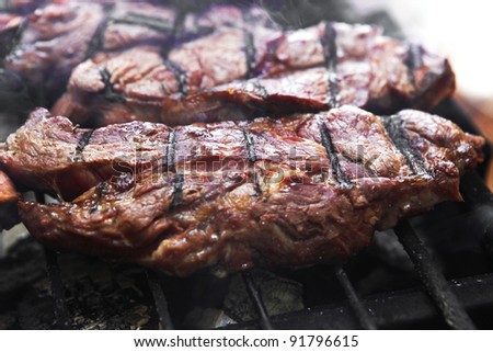 big beef steak on grilling grid over barbecue charcoal