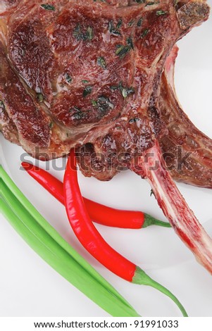 served main course: boned roasted lamb ribs served with green chives and red chili peppers on white dish isolated over white background