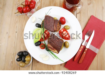 savory food : roast beef garnished with apple juice , green and black olives, red hot peppers on wooden table
