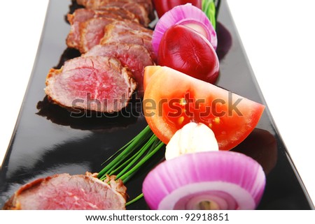 main course : roast red meat slices served on black plate with vegetables on spit isolated on white background