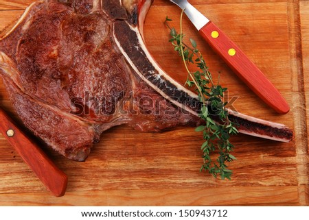 savory : roasted beef spare rib on wooden plate with cutlery and thyme