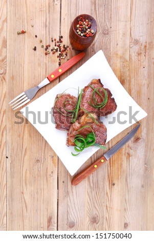 roasted beef meat strips steak on white ceramic plate with hot dry pepper on wood table