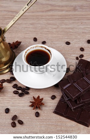sweet hot drink : black Turkish coffee in small white mug with coffee beans spilled on a wooden table with stripes of dark chocolate and copper Arab Cezve full coffee