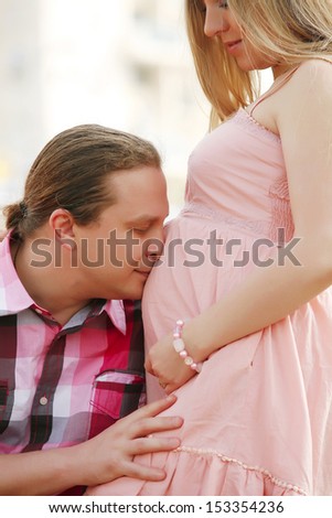 Portrait of a happy young man kisses his pregnant wife belly . outdoor.