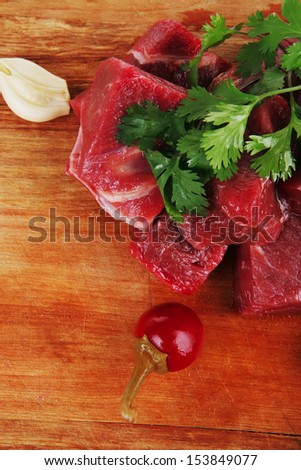 uncooked fresh beef meat chunks on wooden cutting plate with green hot and red peppers isolated over white background