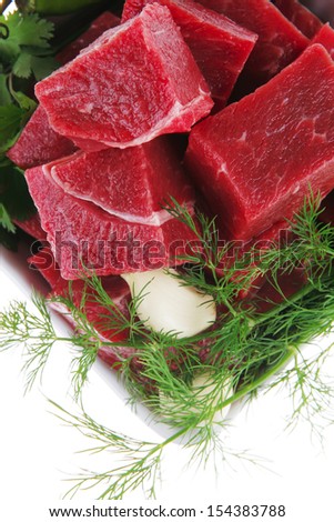 uncooked fresh beef meat chunks on white bowls with green hot peppers and vegetables isolated over white background