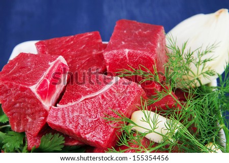 slices of raw fresh beef meat fillet in a white bowls with dill and green peppers serving over blue wooden table
