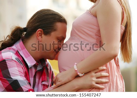 Portrait of a happy young man kisses his pregnant wife belly . outdoor.