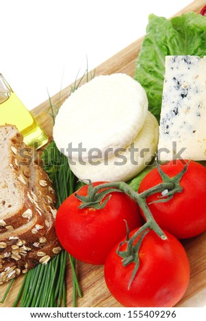 delicatessen cheeses on wooden board with vegetables olive oil and bread isolated over white background