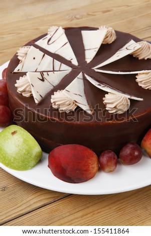 chocolate cream brownie cake topped with white chocolate slice and cream flowers decorated with fruits apple plum and grape on plate on wooden table