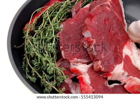 raw beef meat with thyme and pepper on black ceramic pan isolated on white background