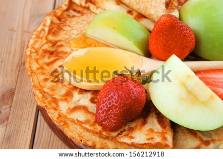 dessert : thin round pancake with honey strawberries and apple on wooden table