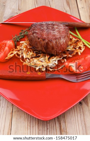 grilled beef fillet medallions on noodles with red hot chili pepper on red plate over wood table
