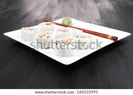Japanese Cuisine - California Roll with Cucumber , Cream Cheese and Raw Salmon inside. Served with wasabi . over black table . on square white plate