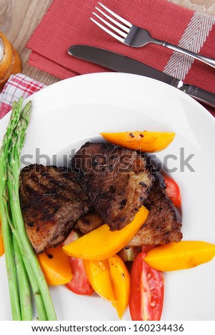 holiday dinner meat food : rare medium roast beef fillet with mango tomatoes and asparagus , served on white dish on red table map over wooden table