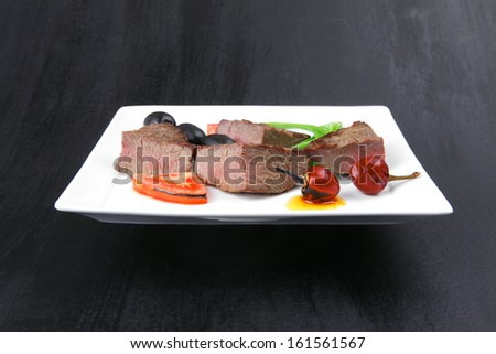 meat food : roasted fillet mignon on white plate with tomatoes apples and chili pepper over black wooden table