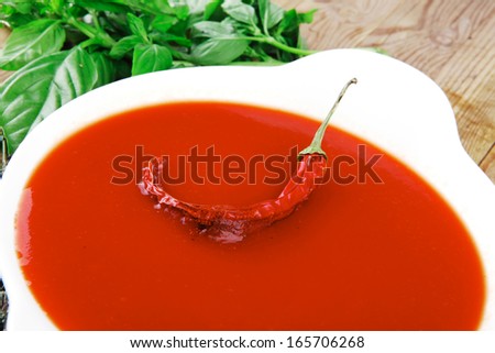 hot fresh diet tomato soup with basil thyme and raw tomatoes in white round bowl over red mat on wood table ready to eat