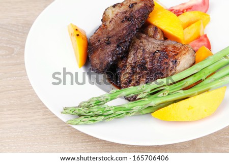 meat food : grilled red beef fillet with mango tomatoes and asparagus , served on white dish over wooden table
