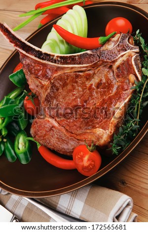 savory : roasted beef spare rib on dark dish with cutlery thyme pepper and tomato on wooden table