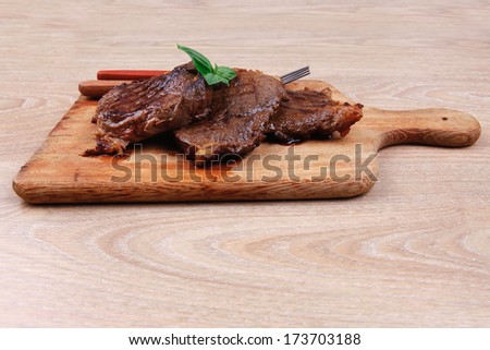 grilled beef on wooden plate with cutlery over table