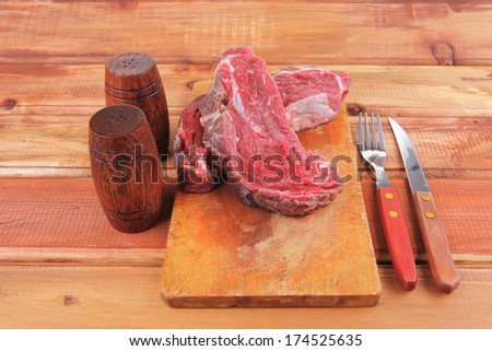 fresh raw uncooked beef fillet mignon entrecote on board prepared for cooking on wood table wtih cutlery and castors