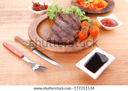 fresh rich juicy grilled beef meat steak fillet entrecote  with marks on wooden plate over table decorated with lettuce salad and cutlery, new york styled cuisine