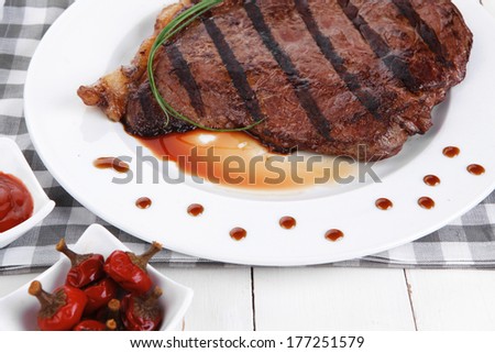 fresh rich juicy grilled beef meat steak fillet entrecote  with marks on white plate over wooden table decorated with sauces and cutlery new york style