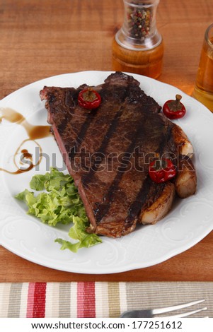 rural design new york meat style beef steak fillet entrecote  on white plate with hot chili pepper served with tea cup ketchup in Gravy boat pepper mill and cutlery on napkin on wooden table