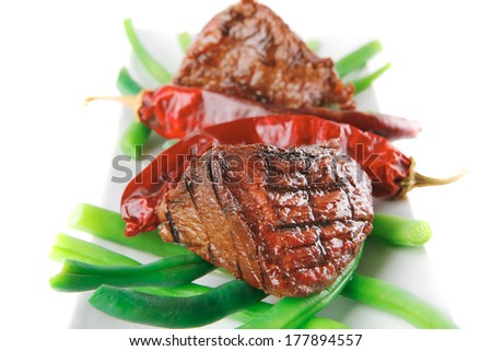 served grilled beef veal fillet entrecote on a white plate with peppers and green peas on long plate isolated on white background